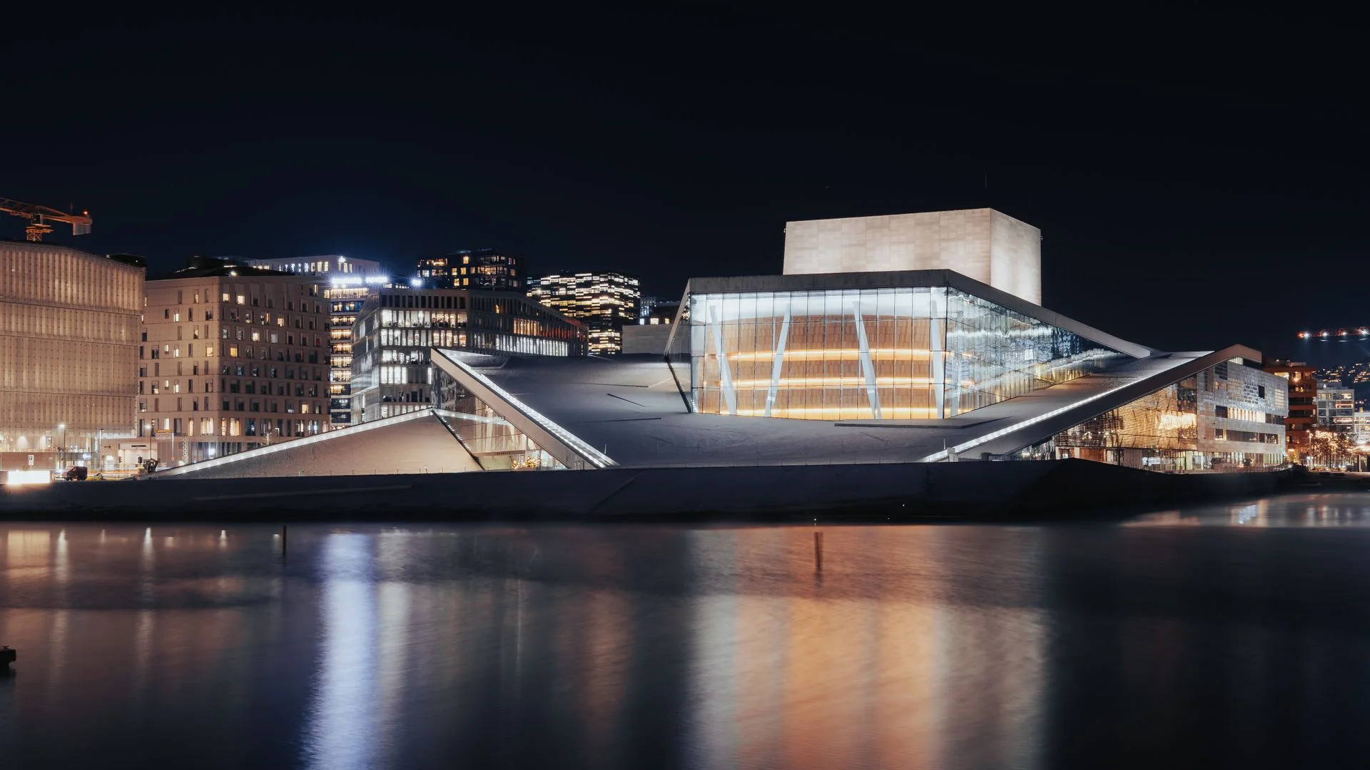Oslo Opera osvětlená v noci, její skleněné foyer zářící nad temnou vodou fjordu
