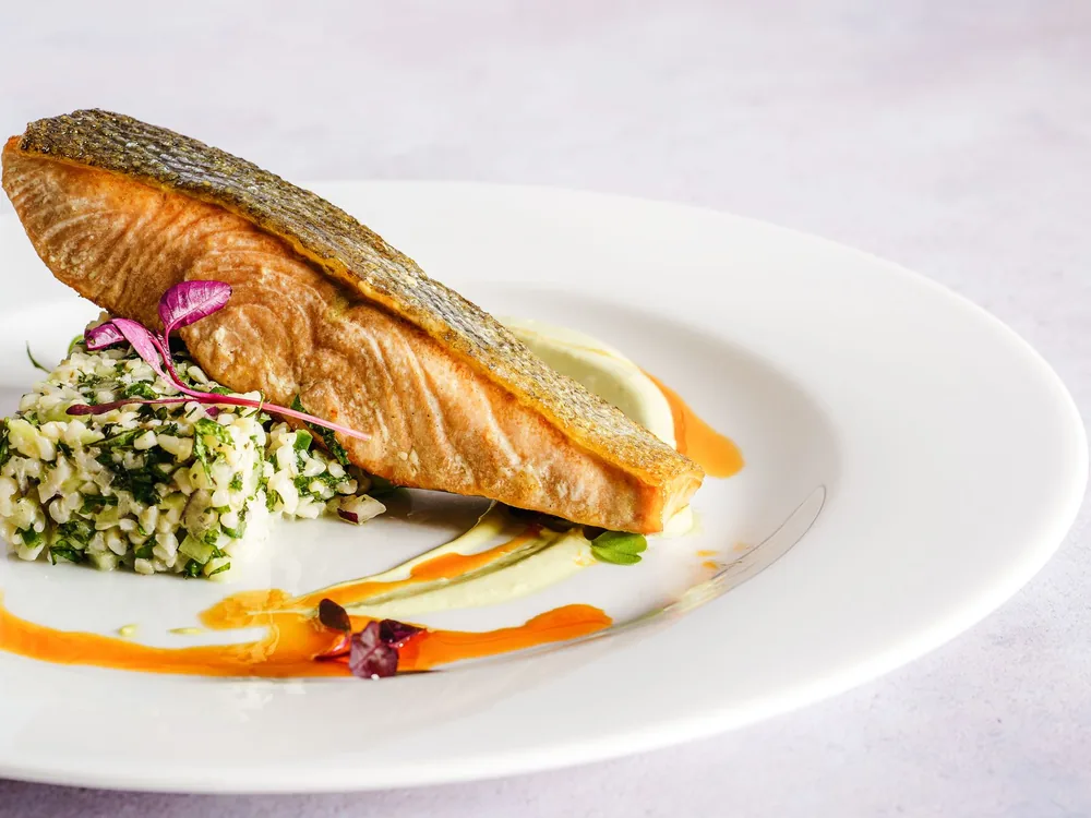 Ein gebratenes Lachsfilet auf einem weißen Teller mit Getreidesalat und einem Hauch von Orangensauce