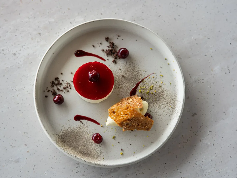 Ein Beerendessert mit rotem Coulis und einem kleinen Kekskrümel auf einem runden grauen Teller