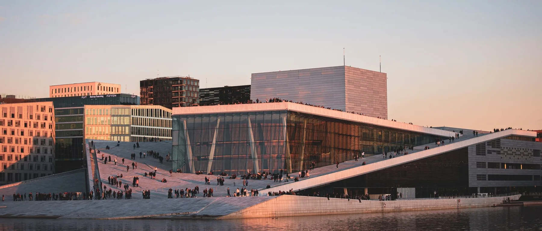 Das Osloer Opernhaus in der Dämmerung, sein weißes Dach neigt sich zum Wasser und fängt das letzte warme Licht ein