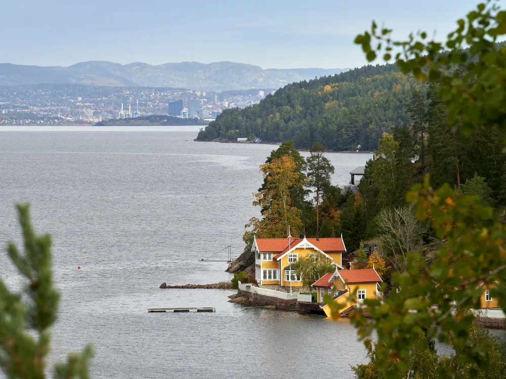 Ein gelbes Holzhaus mit rotem Dach an einem bewaldeten Fjordufer